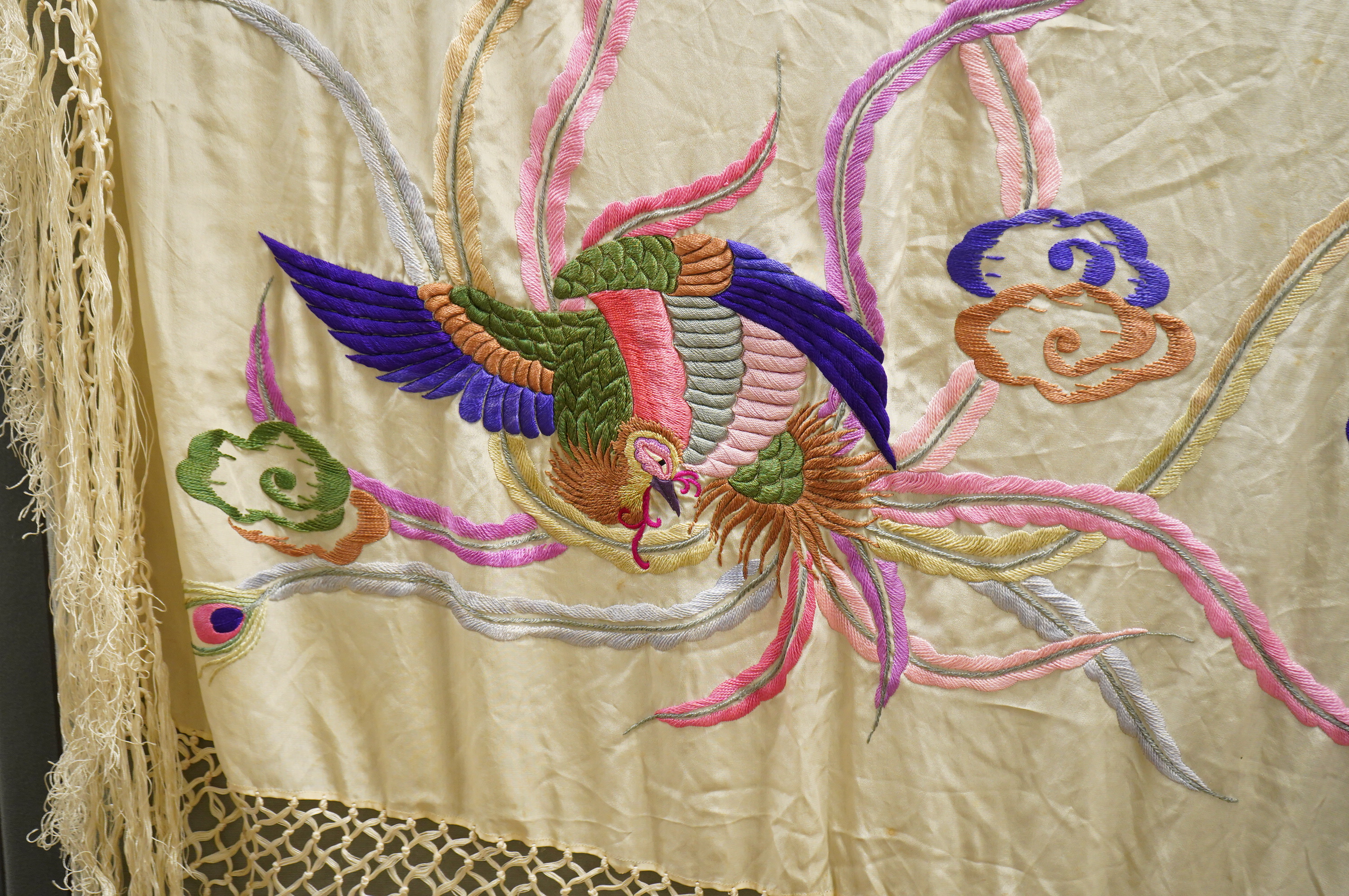 A unusual Chinese 1920’s-30’s cream silk fringed shawl, embroidered with a large central motif of a phoenix in flight, embroidered in bright multi coloured silks. 108cm x 100cm, Condition - there are some stains.